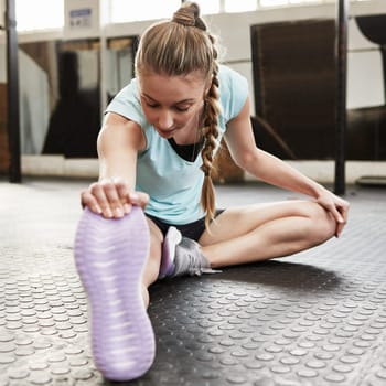 Stretching, fitness and woman in gym for exercise, training and warm up on floor for workout. Health, sports and female person stretch legs in sport center for wellness, performance and flexibility.