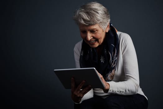 I can get use to this. Studio shot of an cheerful elderly woman standing and using a tablet