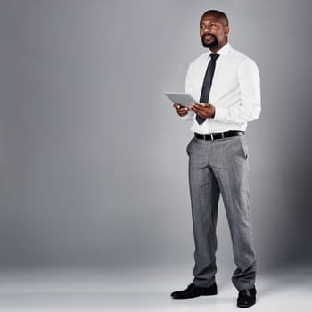 Operating his business through the digital world. Studio shot of a corporate businessman using a digital tablet against a grey background