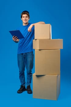 Young male courier in a blue uniform holds parcel in his hands in studio