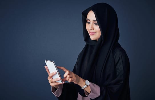 The smartest way of communication for her. Studio shot of a young woman wearing a burqa and using a mobile phone against a gray background