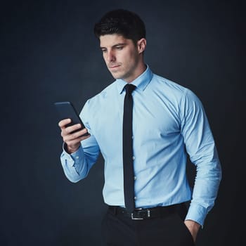 Every executive needs to be within reach. Studio shot of a young businessman texting on a cellphone against a dark background