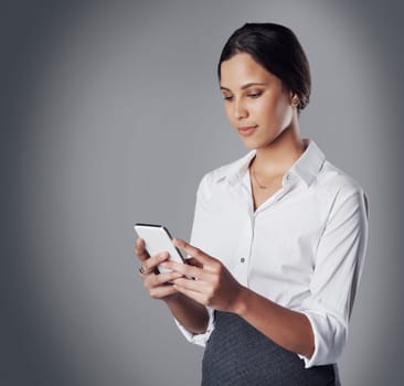 Stay connected, stay ahead of the game. Studio shot of a young businesswoman using a phone against a gray background