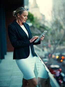 Browsing on the balcony. a mature businesswoman standing outside on the balcony of an office and using a digital tablet