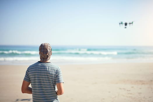 We have liftoff. a focused young man holding a remote control to fly a drone on a beach outside during the day