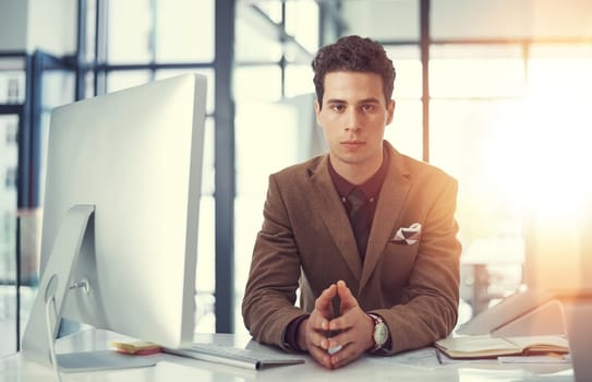 Have a seat. We have work to do. Portrait of a young businessman working at his desk in a modern office