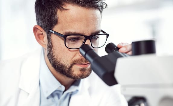 Looking for lifes mysteries. a focused young male scientist looking through a microscope while being seated inside of a laboratory