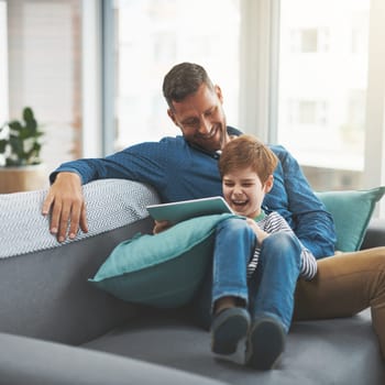 That does look like a fun game. a cheerful little boy browsing on a digital tablet while lying on his fathers lap at home during the day