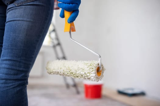 Close-up of woman's hand in glove holding paint roller, ready to paint walls of room. Repair in the apartment