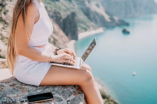 Digital nomad, Business woman working on laptop by the sea. Pretty lady typing on computer by the sea at sunset, makes a business transaction online from a distance. Freelance remote work on vacation