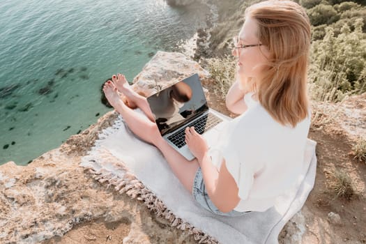 Woman sea laptop. Business woman in yellow hat working on laptop by sea. Close up on hands of pretty lady typing on computer outdoors summer day. Freelance, digital nomad, travel and holidays concept.