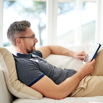 Man, relax and tablet on living room sofa, reading and social media for video, game or movies in home. Mature guy, digital touchscreen and lounge couch for internet blog, news and web app in house.