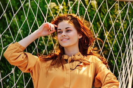 close horizontal photo of a beautiful, red-haired woman lying in a hammock enjoying a rest in an orange dress on a warm summer day. High quality photo