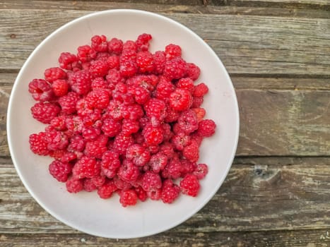 Red fresh raspberries on white rustic wood background. Bowl with natural ripe organic berries