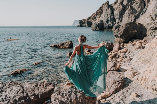 Woman green dress sea. Woman in a long mint dress posing on a beach with rocks on sunny day. Girl on the nature on blue sky background