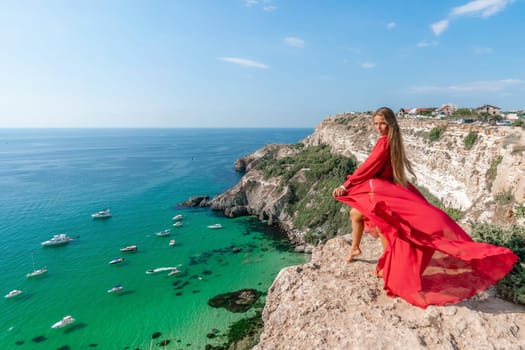 Red Dress Woman sea Cliff. A beautiful woman in a red dress and white swimsuit poses on a cliff overlooking the sea on a sunny day. Boats and yachts dot the background