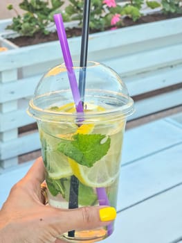 Cold refreshing limonade, mojito or gin tonic in glass, with fresh mint and ice cubes, lime and lemon on wooden table