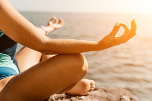 Yoga on the beach. A happy woman meditating in a yoga pose on the beach, surrounded by the ocean and rock mountains, promoting a healthy lifestyle outdoors in nature, and inspiring fitness concept