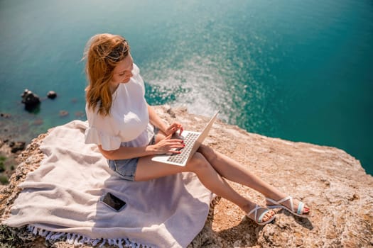 Freelance woman working on a laptop by the sea, typing away on the keyboard while enjoying the beautiful view, highlighting the idea of remote work