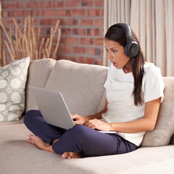 Shocked, home and woman with headphones, laptop and internet connection on sofa listening to music. Female person relax on couch to listen to wow, surprise or fake news announcement online with tech.