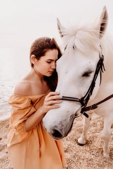 A white horse and a woman in a dress stand on a beach, with the sky and sea creating a picturesque backdrop for the scene