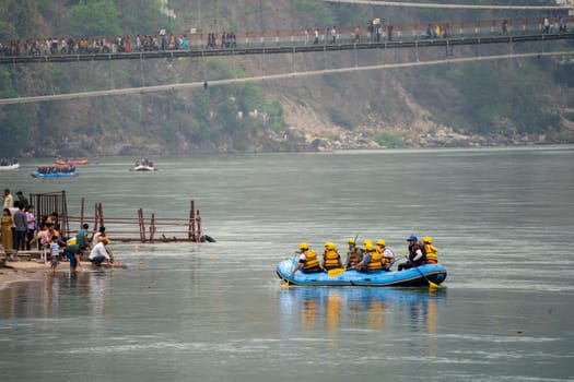 Rishikesh, Haridwar, India - circa 2023: family friends in white water raft in front of temples ghats and the ram setu bridge in holy tourist town of rishikesh