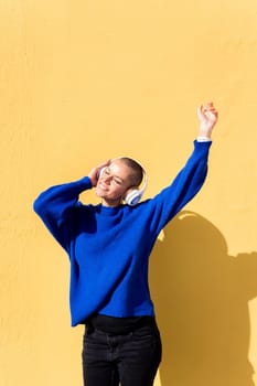 woman dancing happy listening to music in her headphones with a yellow wall in the background, concept of rhythm and positive people, copy space for text
