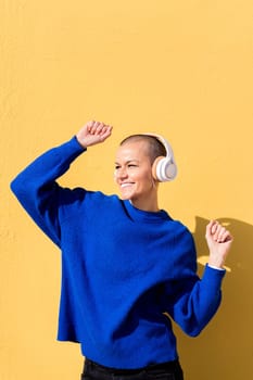 woman smiling happy while dancing listening to music in headphones with a yellow wall in the background, concept of rhythm and positive people, copy space for text