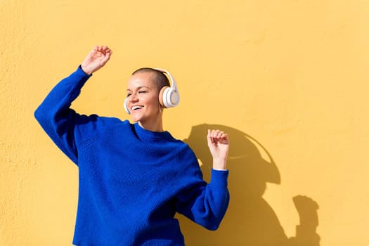 woman smiling happy while dancing listening to music in headphones with a yellow wall in the background, concept of rhythm and positive people, copy space for text