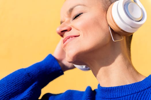 happy woman enjoying music on headphones on yellow background, concept of rhythm and positive people, copy space for text