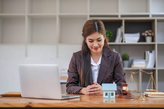 Beautiful Asian businesswoman lawyer sitting at the office holding a pen taking note working on a loan a sample home mallet a laptop