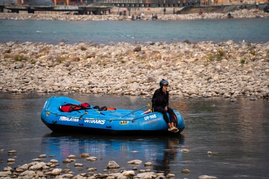 Rishikesh, Haridwar, India - circa 2023: man in black enjoying solo ride on inflatable white water raft while transporting life jackets and waiting for people to board for popular summer adventure sport