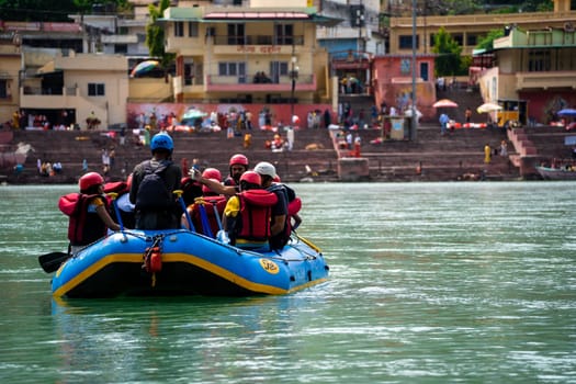 Rishikesh, Haridwar, India - circa 2023: family friends sitting in raft enjoying adventure sports while crossing in front of ghat and temple on the banks of the holy river ganga