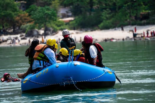 Rishikesh, Haridwar, India - circa 2023: family friends sitting in raft enjoying adventure sports while crossing in front of ghat and temple on the banks of the holy river ganga