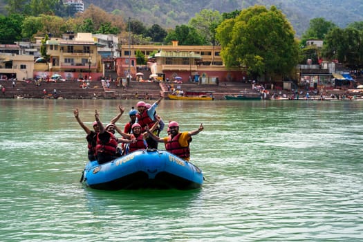 Rishikesh, Haridwar, India - circa 2023: people waving in helments and life jackets enjoying white water river rafting on cool green waters of ganga a popular summer sport