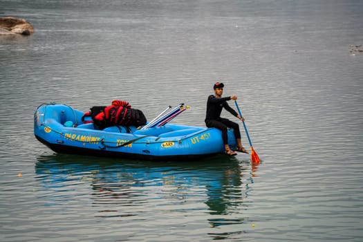 Rishikesh, Haridwar, India - circa 2023: man in black enjoying solo ride on inflatable white water raft while transporting life jackets and waiting for people to board for popular summer adventure sport