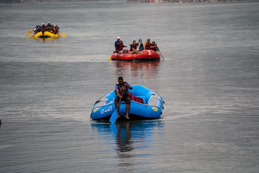 Rishikesh, Haridwar, India - circa 2023: man in black enjoying solo ride on inflatable white water raft while transporting life jackets and waiting for people to board for popular summer adventure sport