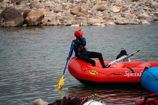 Rishikesh, Haridwar, India - circa 2023: man in black enjoying solo ride on inflatable white water raft while transporting life jackets and waiting for people to board for popular summer adventure sport