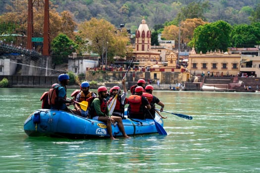 Rishikesh, Haridwar, India - circa 2023: family friends in white water raft in front of temples ghats and the ram setu bridge in holy tourist town of rishikesh