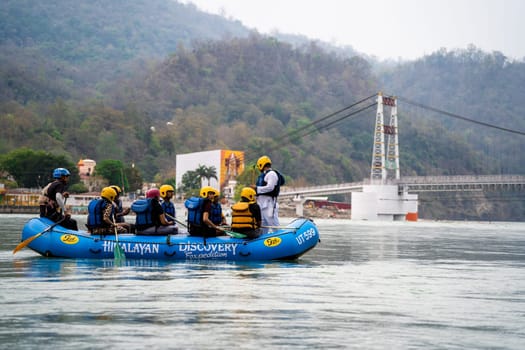 Rishikesh, Haridwar, India - circa 2023: family friends in white water raft in front of temples ghats and the ram setu bridge in holy tourist town of rishikesh