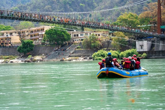 Rishikesh, Haridwar, India - circa 2023: family friends in white water raft in front of temples ghats and the ram setu bridge in holy tourist town of rishikesh