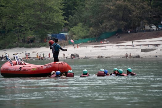 Rishikesh, Haridwar, India - circa 2023: group of people, friends, family floating in blue green cool water of ganga near an inflatable raft and being pulled into it a popular adventure sport