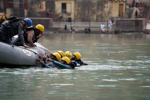 Rishikesh, Haridwar, India - circa 2023: group of people, friends, family floating in blue green cool water of ganga near an inflatable raft and being pulled into it a popular adventure sport