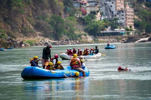 Rishikesh, Haridwar, India - circa 2023: group of people, friends, family floating in blue green cool water of ganga near an inflatable raft and being pulled into it a popular adventure sport