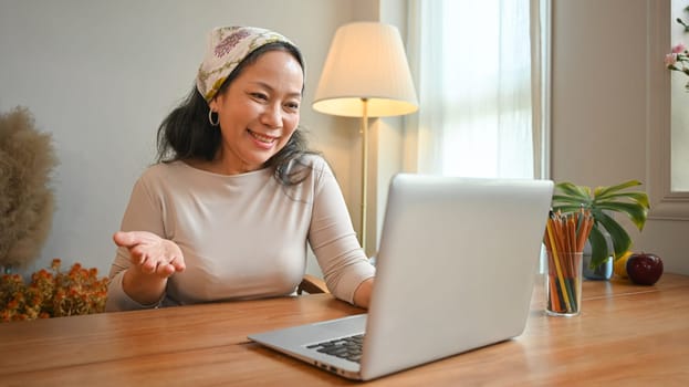 Smiling middle age woman making video call with family or friends on laptop. People, technology and communication concept.