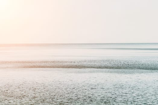 A red burning sunset with the silhouette of a cliff over the sea. Abstract nature summer or spring ocean sea background. Small waves on golden warm water surface with bokeh lights from sun.