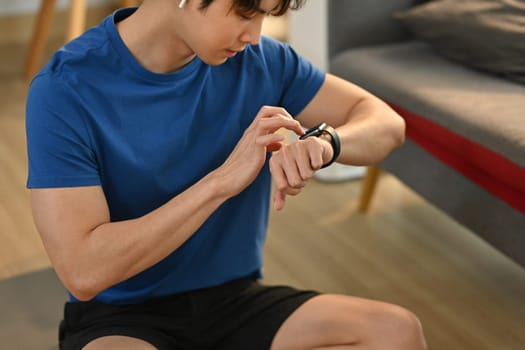 Young fitness asian man checking pulse rate on smartwatch after morning workout. Healthy lifestyle and fitness concept.