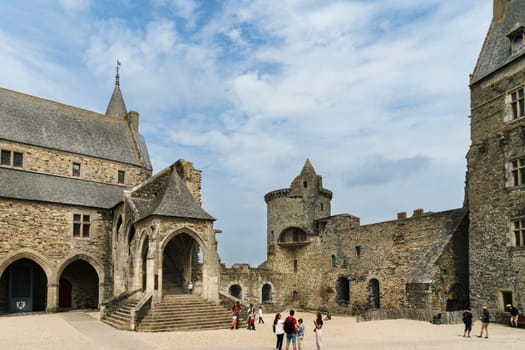 Partial view of the castle of the French town of Vitre on a sunny day and light clouds with tourists in the central courtyard of the castle.