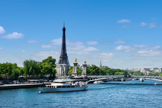 View of the Seine River in Paris with the Eiffel Tower in the background on a summer day with blue sky and white clouds.