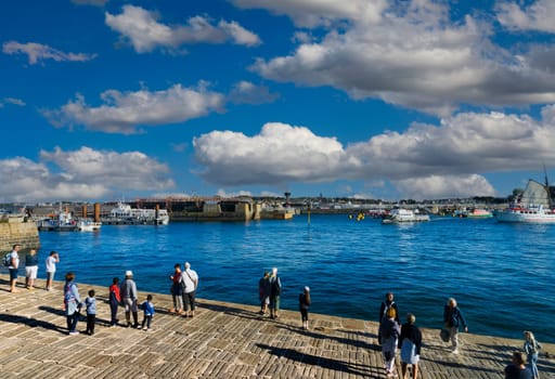 View of the harbor of the French city of Saint Malo with tourists in the foreground and a sunny day with white clouds.